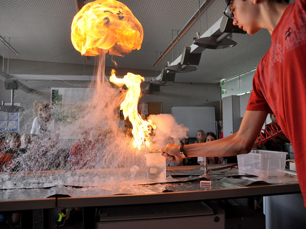 Eine Stichflamme steigt bei einem Versuch über dem Experimentiertisch auf.
